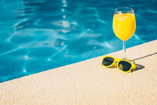 Resort vacation concept - close-up sunglasses and glass of juice on a bright sunny day by the pool - copy space