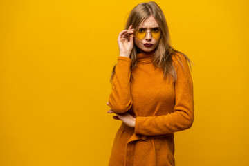 Excited young woman in orange dress, widely smiling, looking at camera. Isolated on yellow background