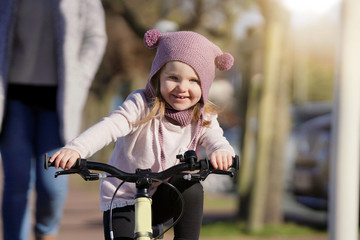 Naklejka premium Adorable young girl in wooly hat riding bike outdoors