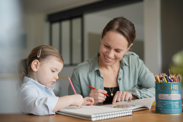 Fototapeta premium Mother and young daughter drawing and reading together at home