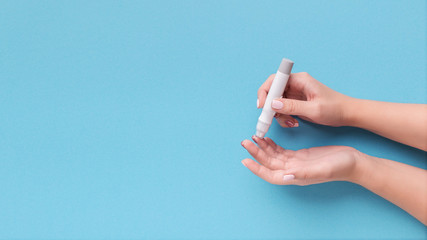 Woman using glucometer on blue background, top view