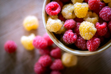 Red and yellow raspberries in a plate on a wooden table