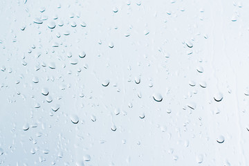 Rain drops on a window glass surface against a white background of rainy clouds.