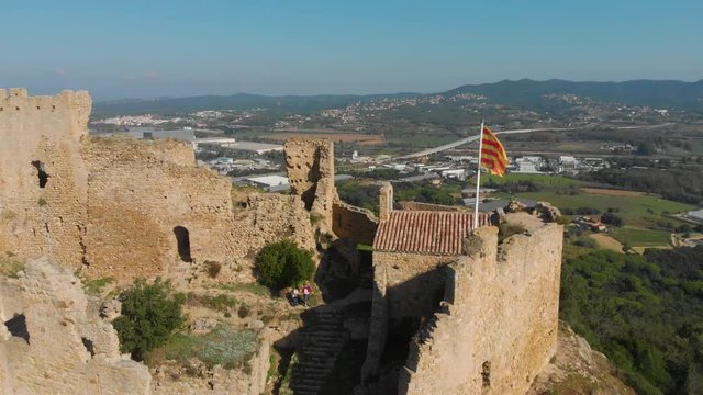 Beautiful landscape of the Palafolls Castle ruins with the Catalonia flag fluttering on a sunny day. Catalonia Spain. Aerial view travelling orbit
