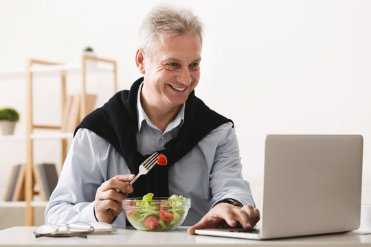 Mature businessman eating salad and working on laptop