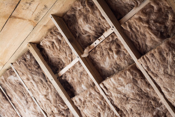 Glass wool in a wooden frame on a inclined wall near the wooden ceiling at attic. Warming the house...