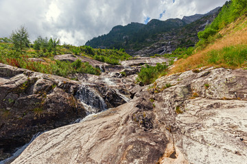 Fototapeta na wymiar Panoramic view of a stream flowing on the steep rocky walls of Monte Rosa in Piedmont, Italy.