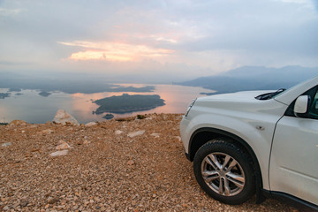 Fototapeta na wymiar white suv car at cliff sunrise over lake on background