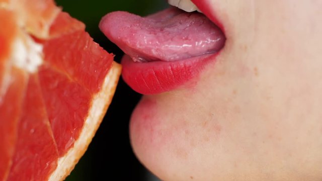 Women's tongue licks a grapefruit. Portrait of a girl with bright red lips that licks a pink grapefruit. Close up, macro