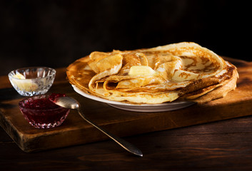 Russian pancakes crepes with butter and raspberry jam on rustic background