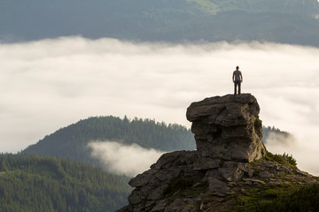 Silhouette of athletic climber tourist on high rocky formation on mountain valley filled with white...