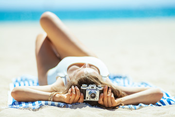 photo camera holding by woman laying on a striped towel