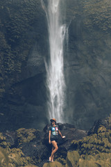 Young woman posing on a great Sekumpul waterfall in the deep rainforest of Bali island, Indonesia.