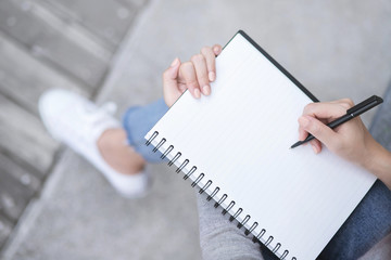 Top view female hands with pen writing on notebook notepad sitting in public park outdoor. Leave copy space  empty write a message.