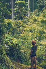 Naklejka premium Young woman posing on a great Sekumpul waterfall in the deep rainforest of Bali island, Indonesia.