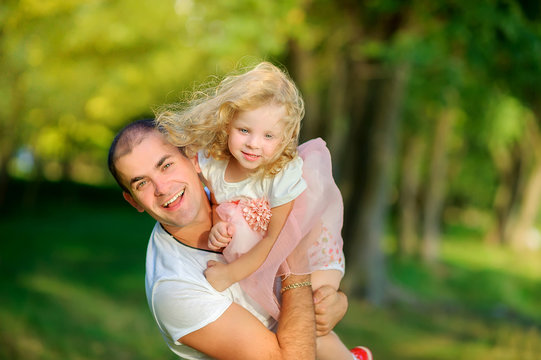 happy dad with little daughter in evening park, holds daughter in her arms and having fun