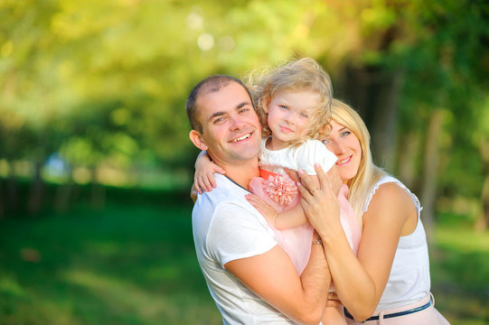 happy family in the evening park, holding a daughter in her arms and smiling