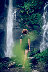 Young woman posing on a great Sekumpul waterfall in the deep rainforest of Bali island, Indonesia.