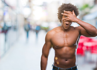 Plakat Afro american shirtless man showing nude body over isolated background peeking in shock covering face and eyes with hand, looking through fingers with embarrassed expression.