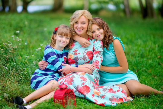 mother with her lovely daughters in the park, sitting on the grass hugging and smiling