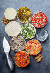 Assortment of French fresh white soft goat cheeses with different tastes topping made with herbs, paprika, indian curry, bruscetta, chives and dried tomatoes