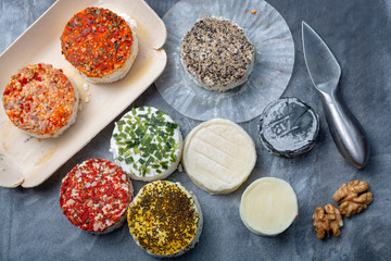 Assortment of French fresh white soft goat cheeses with different tastes topping made with herbs, paprika, indian curry, bruscetta, chives and dried tomatoes