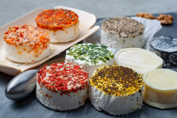 Assortment of French fresh white soft goat cheeses with different tastes topping made with herbs, paprika, indian curry, bruscetta, chives and dried tomatoes