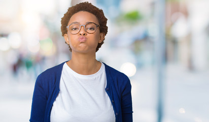 Young beautiful african american woman wearing glasses over isolated background puffing cheeks with funny face. Mouth inflated with air, crazy expression.