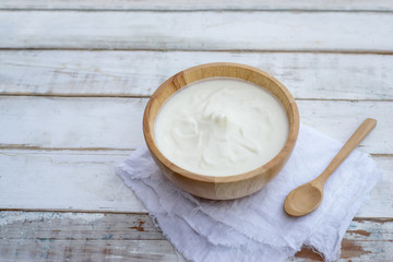 Greek yogurt or sour cream in a wooden bowl on dark table top view. Healthy food nutrition.