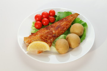 Fish with potatoes tomatoes lettuce and lemon on plate