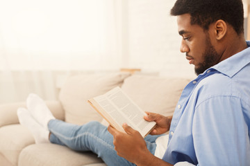 Black male student reading book at home