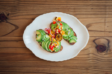 Top shot of sliced avocado on rye toast with a rustic tomato, yellow pepper and red onion salsa and burnt lime, on a wooden back
