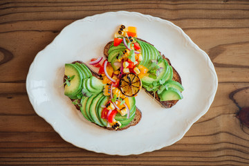Top shot of sliced avocado on rye toast with a rustic tomato, yellow pepper and red onion salsa and burnt lime, on a wooden back