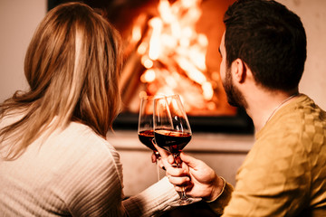 Chill couple having wine drinks and looking at fire burning in fireplace, in cosy living room