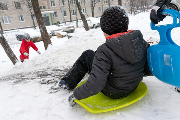Fototapeta na wymiar A boy of seven years old rides the slide , down the hill on green ice sled. Concept of winter activities, recreation and children's entertainment
