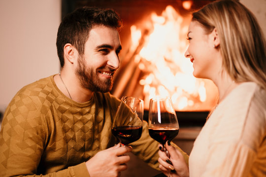 Romantic couple smiling and enjoying a drink, having a glass of wine by the fireplace