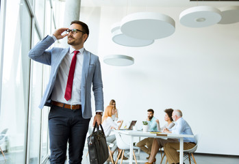 Young businessman leaves a meeting while other people stay in office