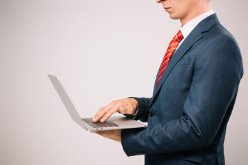 cropped view of businessman in suit using laptop isolated on grey