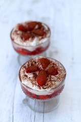 Strawberries with whipped cream and cocoa powder in decorative glass bowls. White rustic table, selective focus.