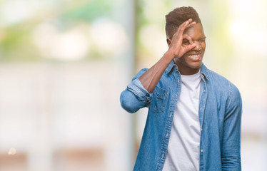Young african american man over isolated background doing ok gesture with hand smiling, eye looking through fingers with happy face.