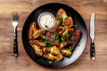 Baked chicken wings in Mexican with curry seasoning and parsley on a black plate, on a wooden background. side view, copy space, top view