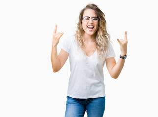 Beautiful young blonde woman wearing glasses over isolated background shouting with crazy expression doing rock symbol with hands up. Music star. Heavy concept.