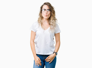 Beautiful young blonde woman wearing glasses over isolated background making fish face with lips, crazy and comical gesture. Funny expression.