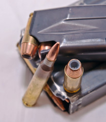 A loaded handgun magazine with 40 caliber bullets and a loaded rifle magazine with .223 caliber bullets along with each of those bullets on the magazines on a white background