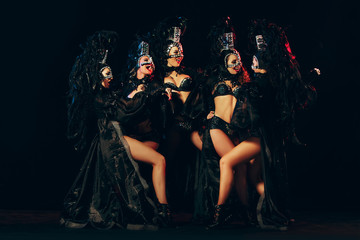 The group of young happy smiling beautiful female dancers with carnival dresses posing on black studio background