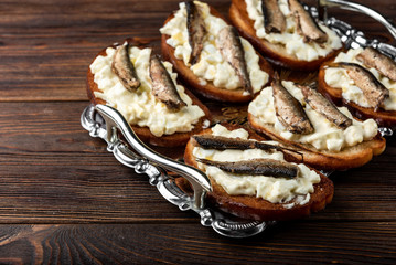 Sandwich with sprats, eggs and mayonnaise on wooden background.