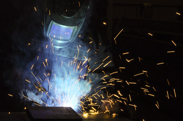  Welder on the production of weld metal. Sparks fly, smoke