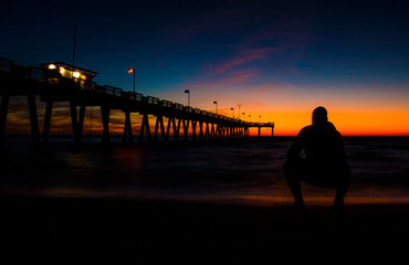 silhouette of man walking on pier at sunset