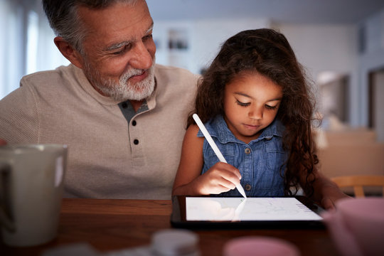 Senior Hispanic Man With His Young Granddaughter Using Stylus And Tablet Computer, Front, Close Up