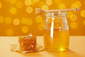 Jar with honey and fresh comb on table against blurred background